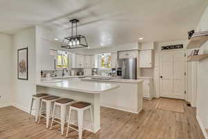 Kitchen featuring recessed lighting, a breakfast bar area, stainless steel refrigerator with ice dispenser, light countertops, and white cabinets