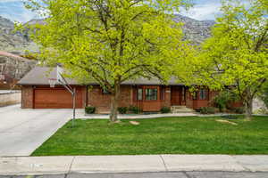 Ranch-style home featuring a garage, a mountain view, a front lawn, and driveway