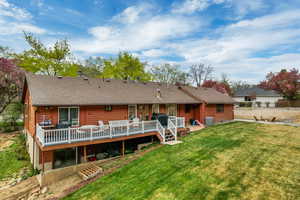Rear view of house featuring a deck, a yard, fence, roof with shingles, and central AC