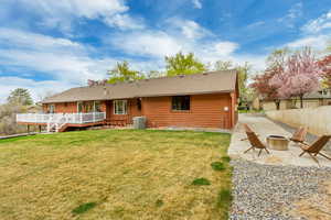 Rear view of house with a fire pit, a patio, a wooden deck, central air condition unit, and a lawn