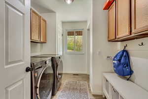 Clothes washing area featuring light wood finished floors, washer and clothes dryer, cabinet space, and baseboards