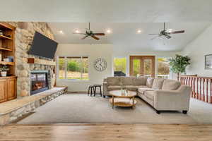 Living room featuring wood finished floors, a ceiling fan, a fireplace, and vaulted ceiling