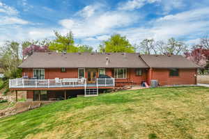 Back of property featuring a lawn, a deck, and a shingled roof