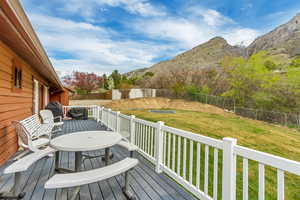 Deck with a mountain view, a fenced backyard, outdoor dining space, and a lawn