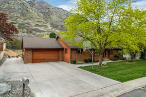 Single story home featuring brick siding, a garage, driveway, a mountain view, and a front lawn