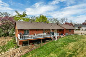 Rear view of property featuring cooling unit, a deck, a yard, and roof with shingles