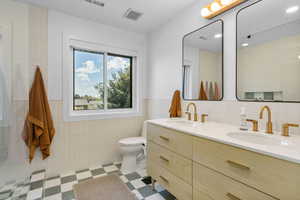 Full bath with double vanity, tile walls, toilet, and a sink