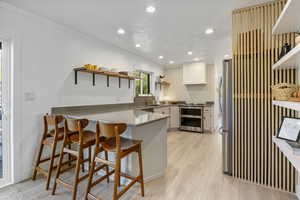 Kitchen featuring freestanding refrigerator, open shelves, a sink, range with two ovens, and a peninsula