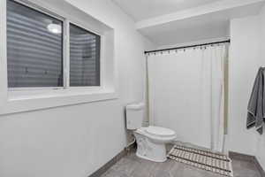 Bathroom with toilet, shower / bathtub combination with curtain, and baseboards