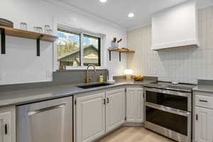 Kitchen featuring open shelves, appliances with stainless steel finishes, white cabinets, a sink, and light wood-type flooring