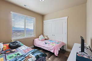 Bedroom with dark wood-style flooring, visible vents, baseboards, and a closet
