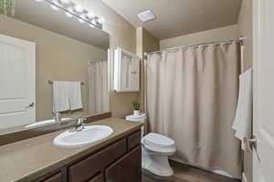 Bathroom featuring wood finished floors, a shower with shower curtain, toilet, vanity, and a textured ceiling