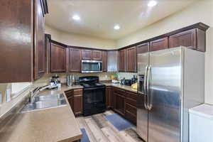 Kitchen with light wood finished floors, recessed lighting, a sink, appliances with stainless steel finishes, and dark brown cabinets