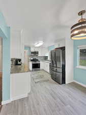Kitchen featuring light wood finished floors, light stone countertops, stainless steel appliances, white cabinetry.