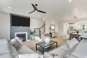 Living room with ceiling fan, a glass covered fireplace, light wood-type flooring, recessed lighting, and stairs