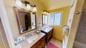 Full bath featuring vaulted ceiling, two vanities, tile patterned flooring, and a sink