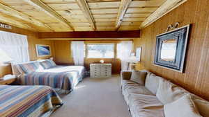 Carpeted bedroom featuring beamed ceiling, wooden walls, wooden ceiling, and multiple windows