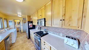 Kitchen featuring appliances with stainless steel finishes, visible vents, light countertops, light brown cabinetry, and washer and dryer