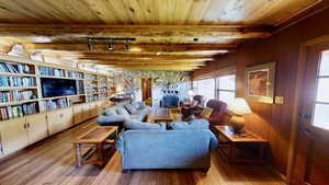 Living room featuring wood ceiling, hardwood / wood-style flooring, beamed ceiling, rail lighting, and wooden walls
