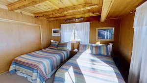 Carpeted bedroom featuring wood walls, beamed ceiling, and wood ceiling