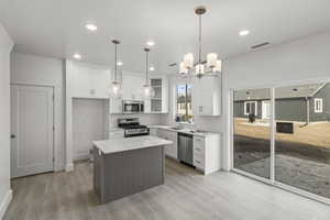Kitchen with white cabinetry, a sink, appliances with stainless steel finishes, light wood-style floors, and light countertops