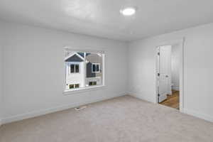 Primary bedroom featuring light colored carpet, large window, and baseboards (View is different)
