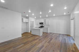 Kitchen featuring stainless steel appliances, wood finished floors, white cabinets, and an island with sink