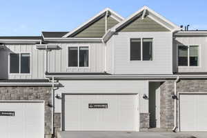 Townhome / multi-family property featuring a garage, board and batten siding, and stone siding