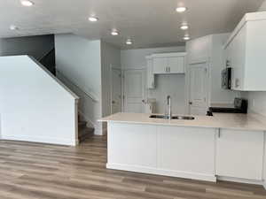 Kitchen with stainless steel microwave, a sink, black range with gas stovetop, light wood-style flooring, and a peninsula