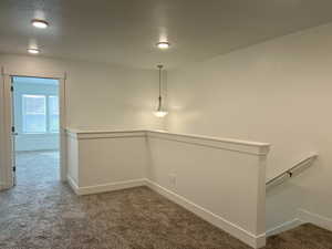 Interior space featuring an upstairs landing, a textured ceiling, carpet, and baseboards