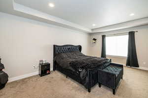 Carpeted bedroom with a raised ceiling, recessed lighting, and baseboards