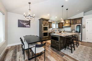 Kitchen with dark brown cabinetry, a chandelier, vaulted ceiling, and appliances with stainless steel finishes