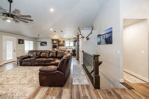 Living area with baseboards, wood finished floors, ceiling fan with notable chandelier, and vaulted ceiling