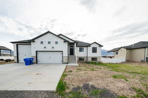 View of front of house with driveway, stone siding, board and batten siding, an attached garage, and fence