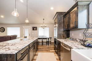 Kitchen featuring light stone counters, lofted ceiling, appliances with stainless steel finishes, dark brown cabinetry, and light wood-type flooring