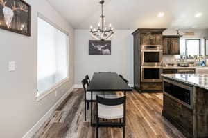 Kitchen with a chandelier, appliances with stainless steel finishes, vaulted ceiling, dark brown cabinets, and dark wood-style flooring