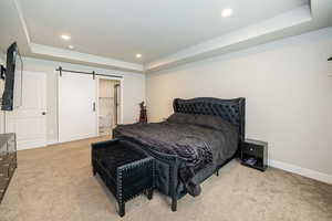 Carpeted bedroom featuring recessed lighting, baseboards, a barn door, and a tray ceiling
