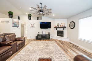Living area featuring visible vents, vaulted ceiling, a fireplace, wood finished floors, and a ceiling fan