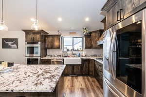 Kitchen featuring dark brown cabinetry, light stone countertops, stainless steel appliances, a sink, and light wood-type flooring