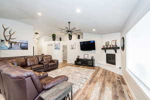 Living area with recessed lighting, wood finished floors, a large fireplace, ceiling fan, and lofted ceiling