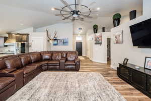 Living room featuring baseboards, ceiling fan, light wood-style flooring, and vaulted ceiling
