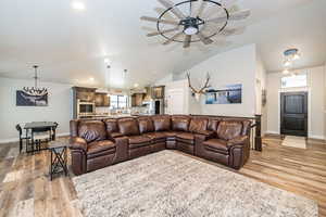 Living room with vaulted ceiling, baseboards, light wood-style flooring, and ceiling fan with notable chandelier