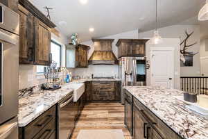 Kitchen with a sink, custom range hood, dark brown cabinetry, appliances with stainless steel finishes, and lofted ceiling