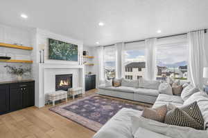 Living room with a brick fireplace, recessed lighting, a textured ceiling, and light wood-type flooring