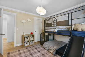 Bedroom featuring baseboards, ornamental molding, a textured ceiling, and wood finished floors