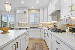 Kitchen featuring white cabinets, custom range hood, a sink, stainless steel gas stovetop, and light wood-type flooring