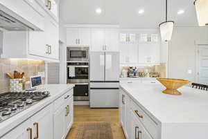Kitchen with wall chimney range hood, tasteful backsplash, stainless steel appliances, and light wood-style floors