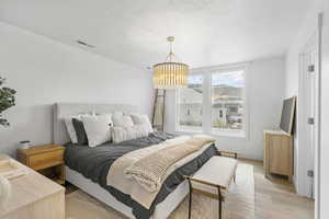 Bedroom featuring a textured ceiling, visible vents, a chandelier, and light wood-style floors