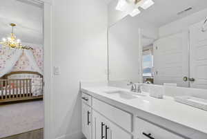 Ensuite bathroom with an inviting chandelier, connected bathroom, vanity, visible vents, and baseboards
