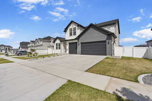 View of front of property featuring a front yard, a garage, a residential view, concrete driveway, and fence